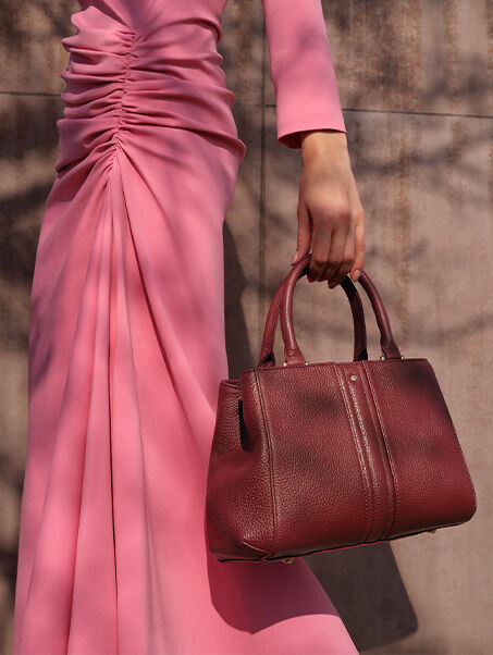 Woman outdoors leaning against a wall wearing a pink draped dress and a red leather handbag with double handles | GEOX | GEOX